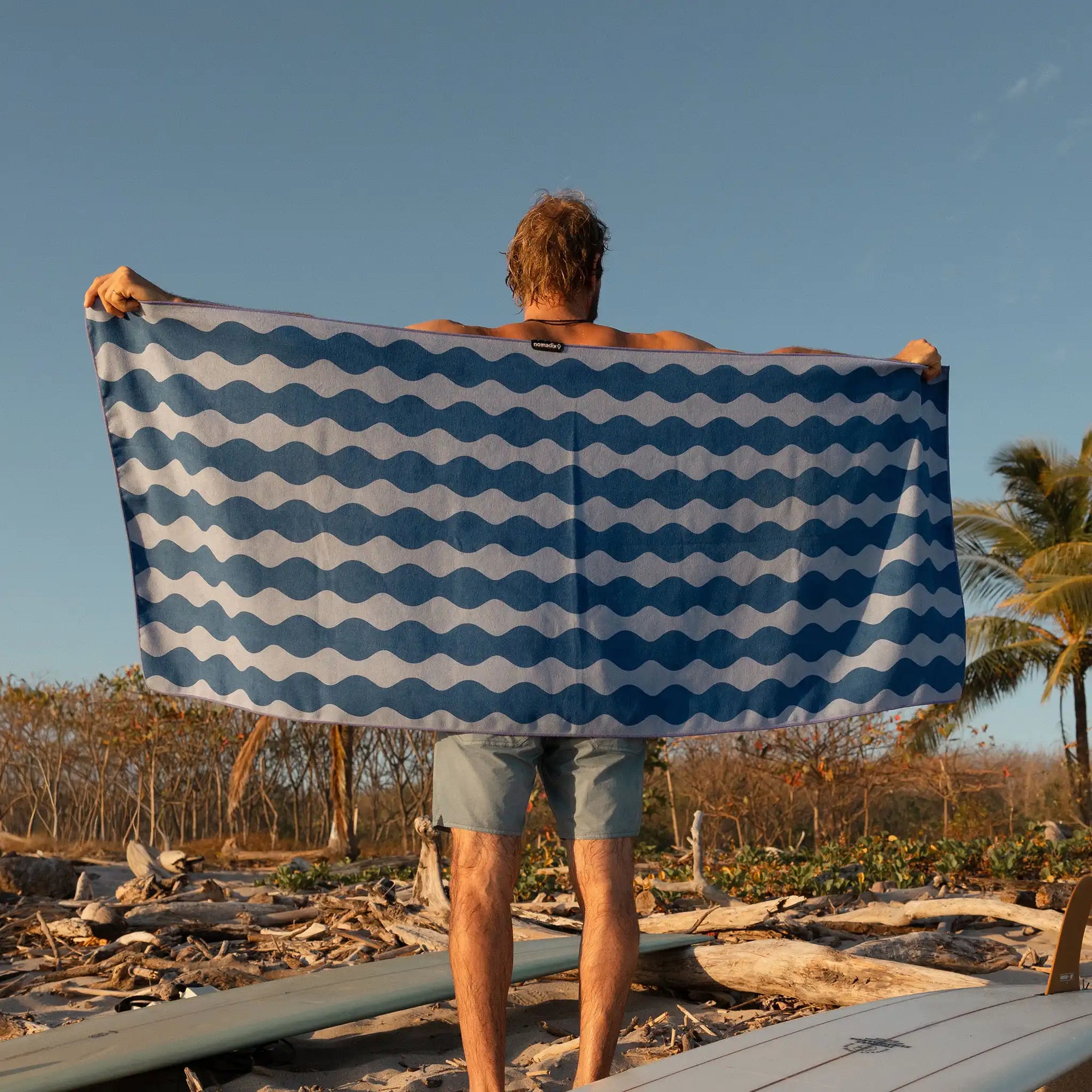 Person holding blue and white wave-patterned beach towel outdoors at sunset