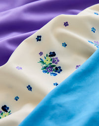 Close-up of cream floral-printed fabric with blue and purple flower motifs alongside solid color fabrics