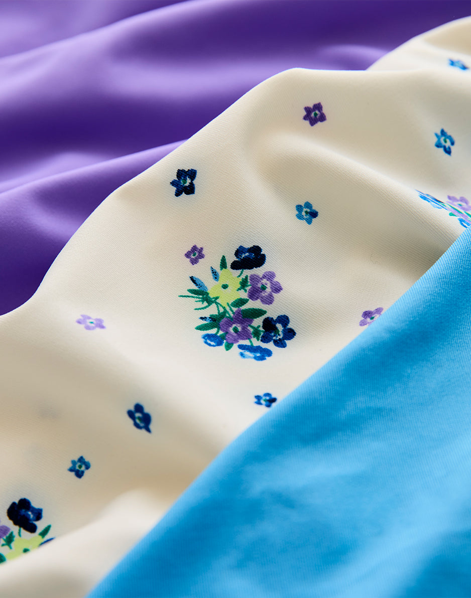 Close-up of cream floral-printed fabric with blue and purple flower motifs alongside solid color fabrics