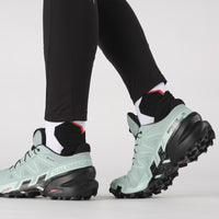Trail running shoes with mint green upper and aggressive black lugged outsole, on-model side view