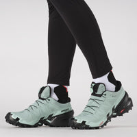 Women's trail running shoes in mint green and black, on-model side view showing aggressive lug sole