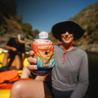 Hand holding a colorful gradient can koozie on a river rafting trip outdoors