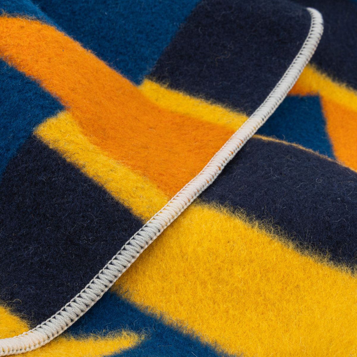 Close-up detail of a wool blanket showing geometric plaid pattern with cream stitched edge binding