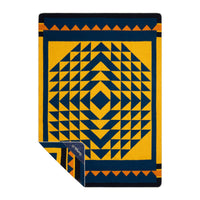 Geometric patterned blanket in gold and navy with triangular border, corner folded back showing reverse side