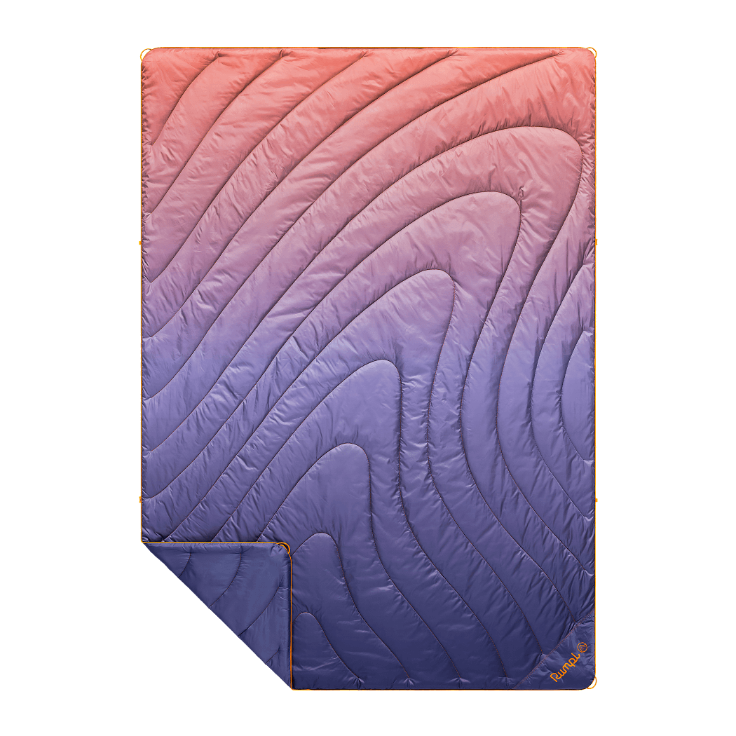 Quilted puffy blanket with gradient fade pattern from coral to navy, shown folded with corner detail