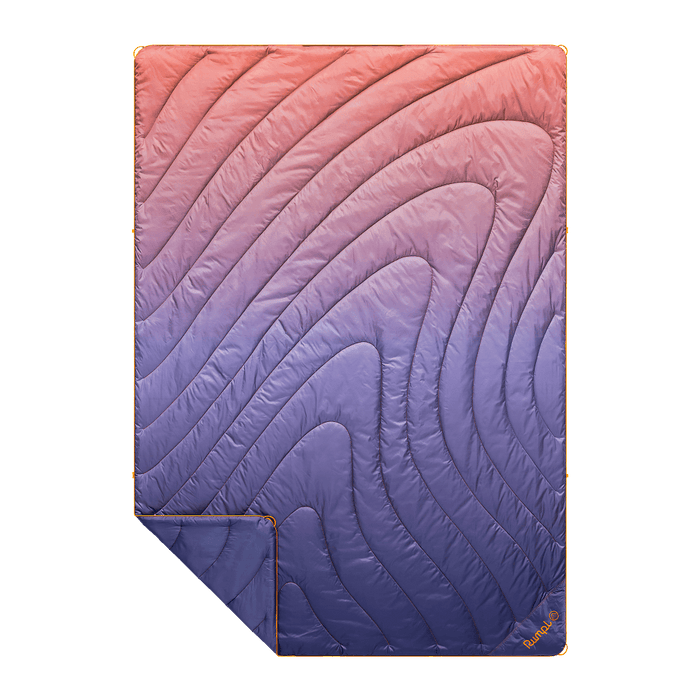 Quilted puffy blanket with gradient fade pattern from coral to navy, shown folded with corner detail