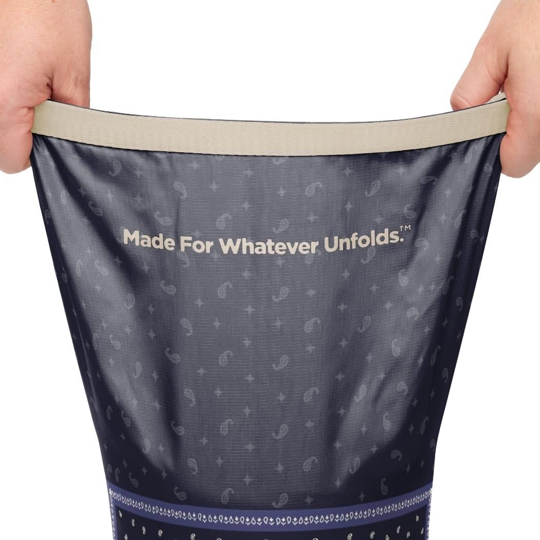 Hands stretching open a navy paisley-print puffy blanket showing interior lining and brand slogan