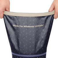 Hands stretching open a navy paisley-print puffy blanket showing interior lining and brand slogan