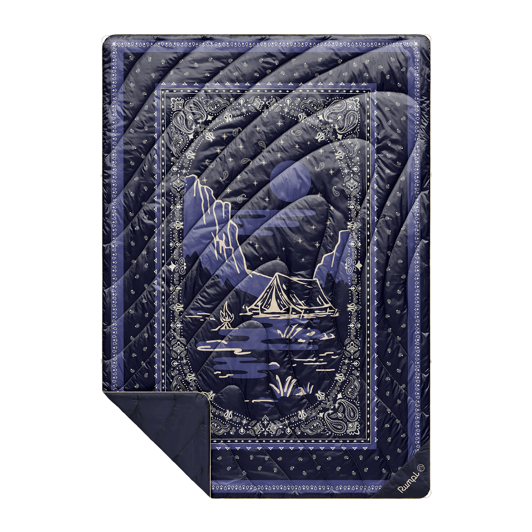 Quilted puffy blanket in navy blue bandana print with mountain camping scene graphic, flat lay view