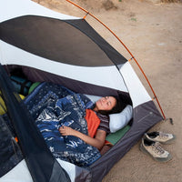 Person sleeping in tent wrapped in navy blue paisley-print puffy blanket, camping lifestyle shot