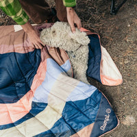 Puffy outdoor blanket with blue coral geometric pattern spread outdoors with fluffy white dog