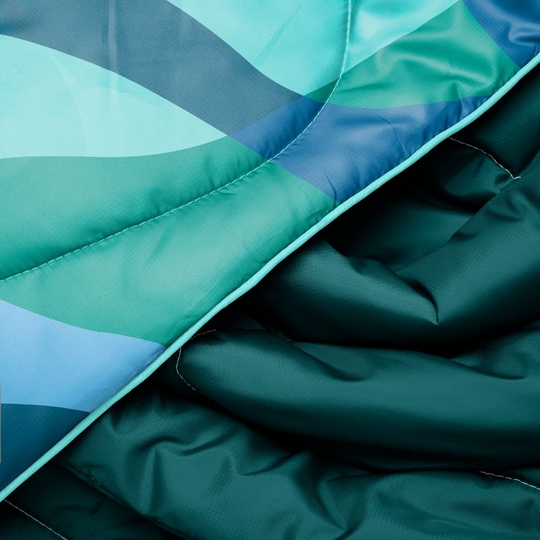 Quilted puffy blanket with teal and blue geometric pattern, showing fabric texture and stitching details
