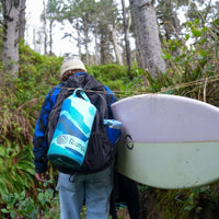 Person wearing backpack with blue geometric patterned puffy blanket attached in forest setting