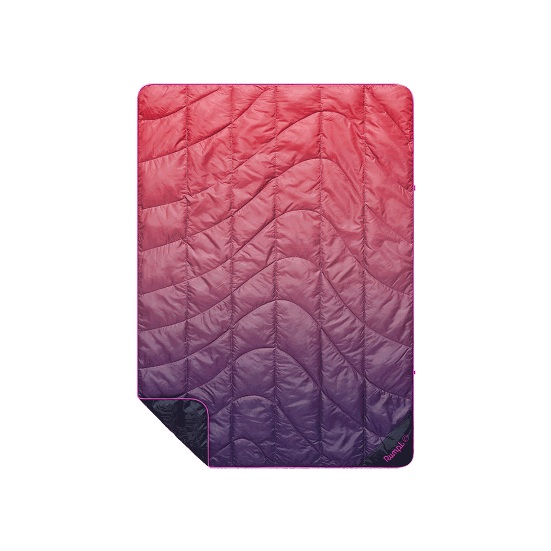 Quilted puffy travel blanket with pink-to-purple ombre gradient and wave-pattern stitching, flat lay view