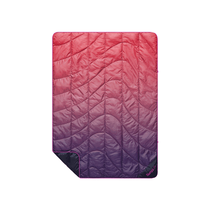 Quilted puffy travel blanket with pink-to-purple ombre gradient and wave-pattern stitching, flat lay view