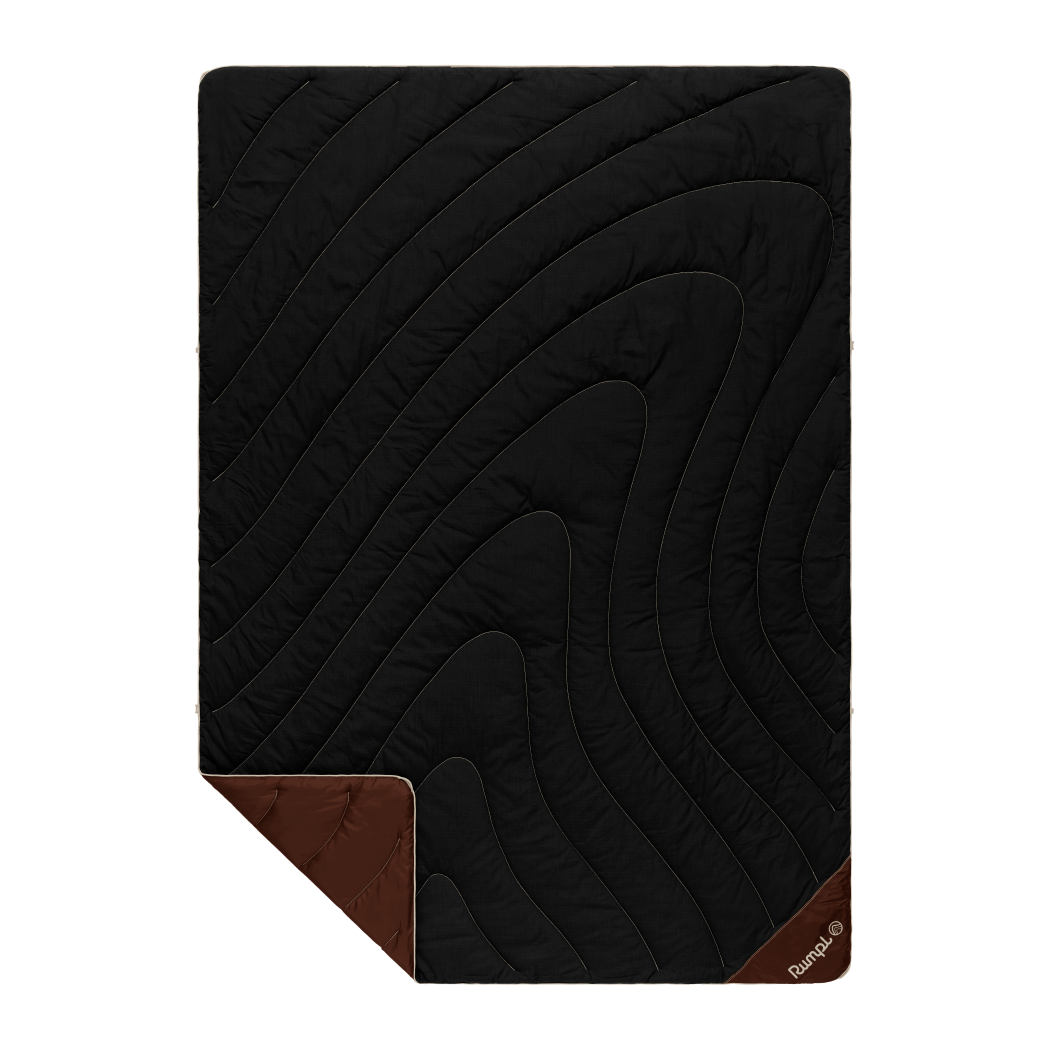 Black quilted camping blanket with diagonal stitching pattern and brown corner accents, flat lay view