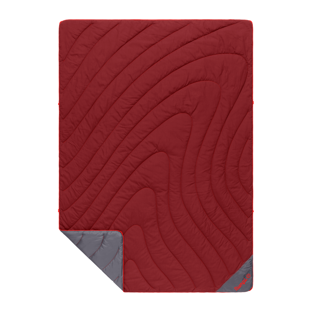 Red quilted puffy blanket with curved stitching pattern and gray corner fold showing reverse side