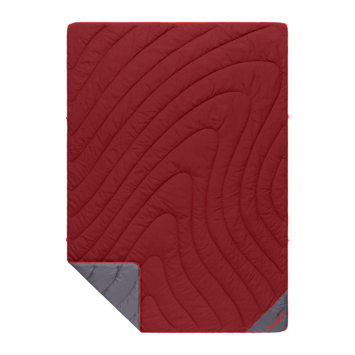 Red quilted puffy blanket with curved stitching pattern and gray corner fold showing reverse side