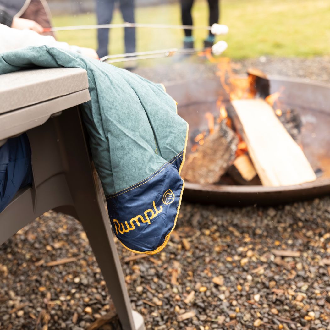 Puffy quilted blanket in sage green and navy draped over outdoor chair near campfire