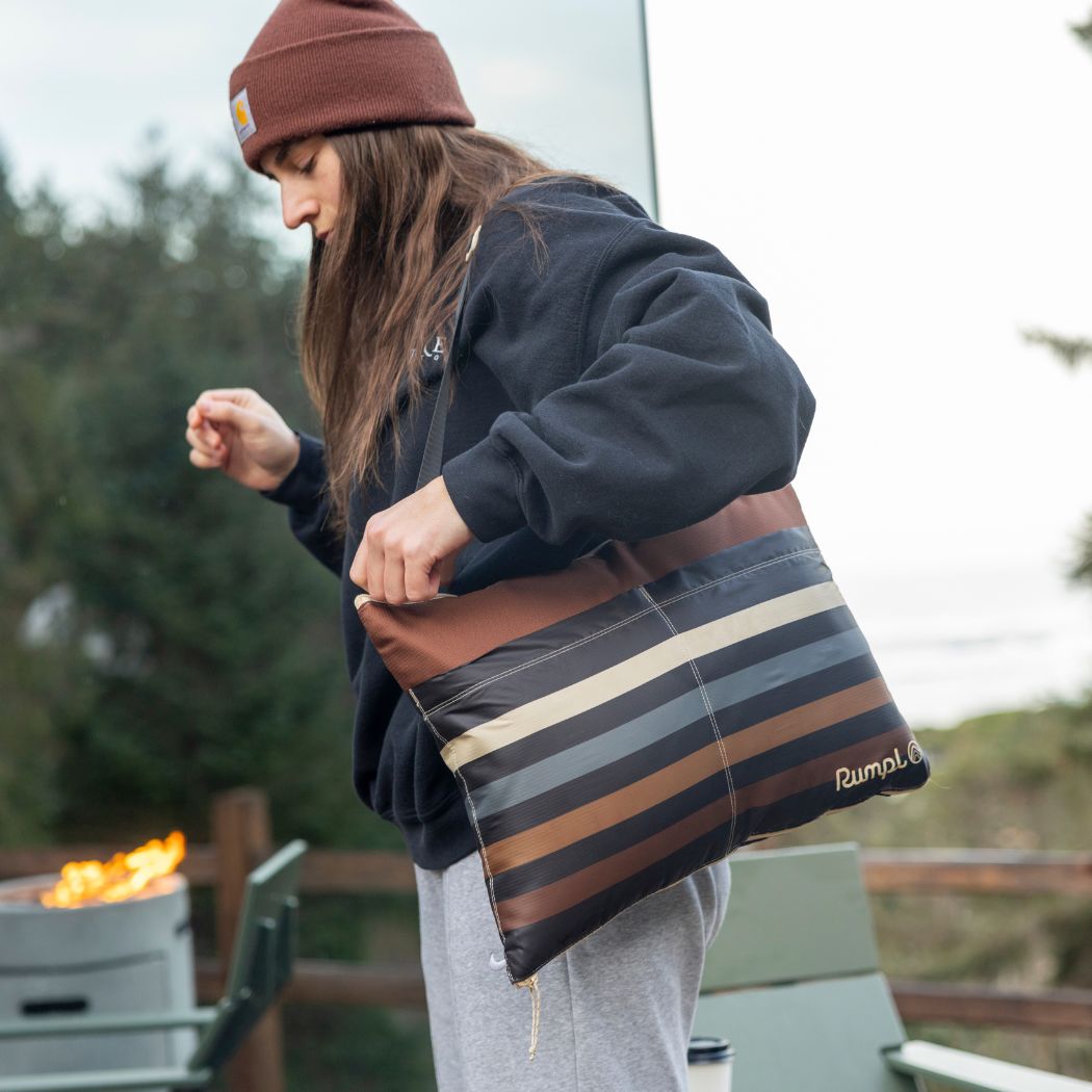 Person carrying striped outdoor blanket with brown and neutral tones in outdoor setting