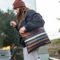 Person carrying striped outdoor blanket with brown and neutral tones in outdoor setting
