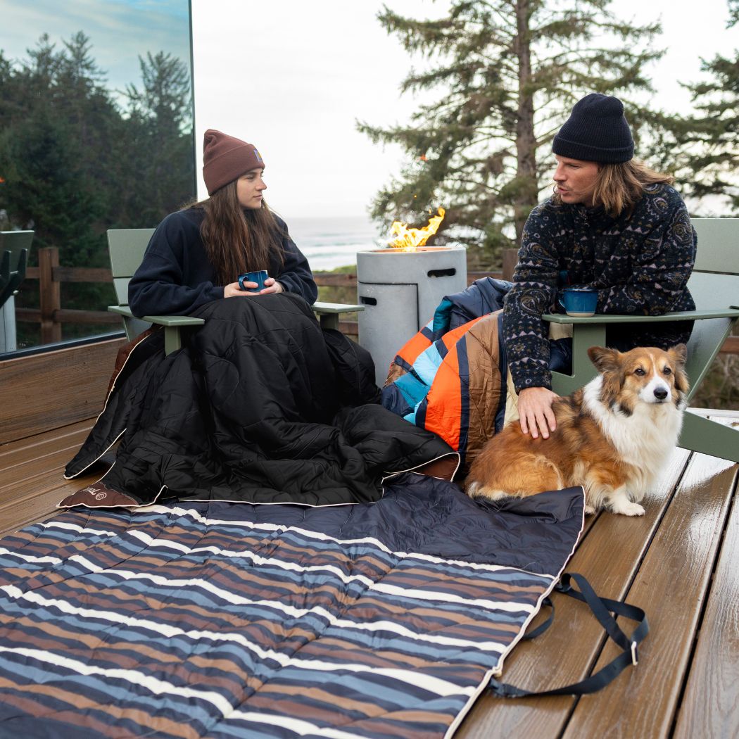 Striped outdoor mat with two people camping on deck with dog and fire pit