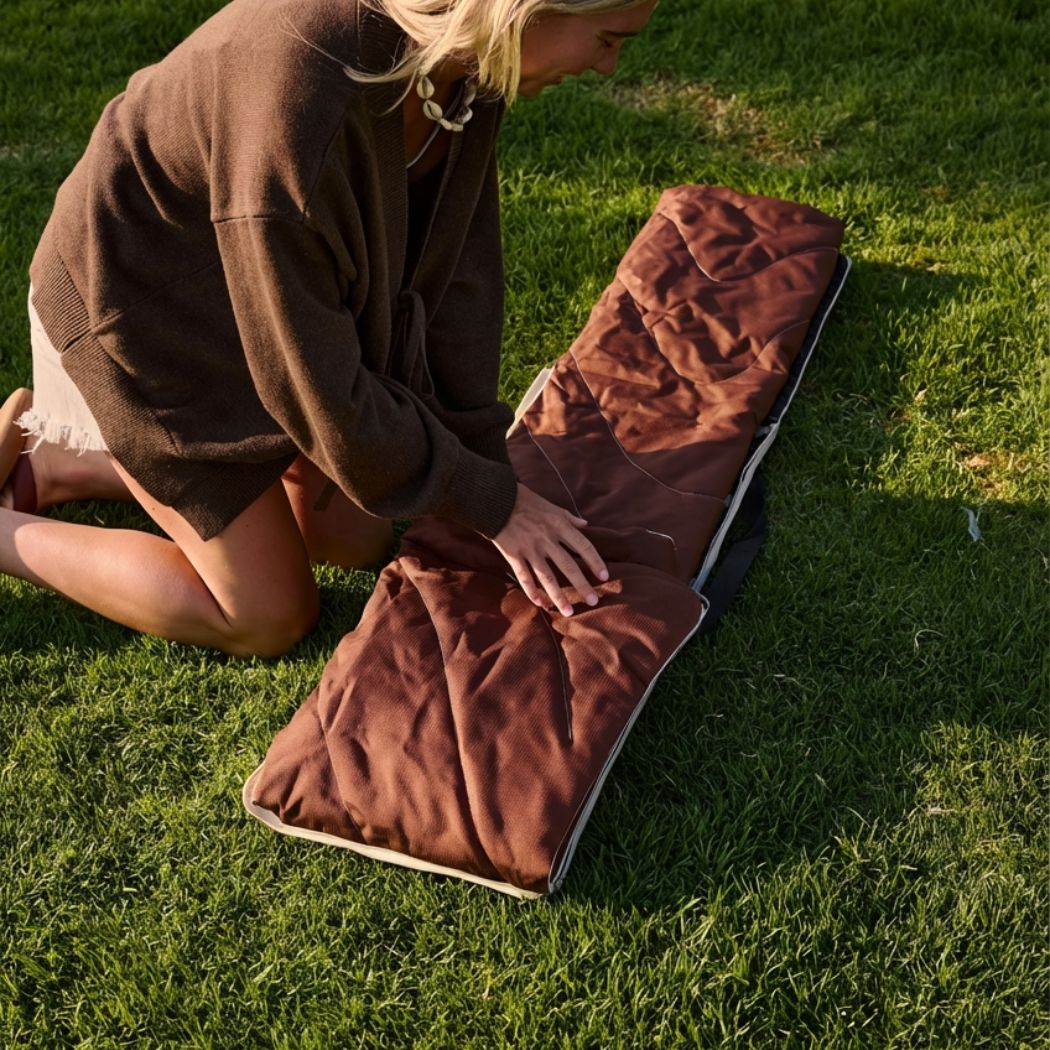 Brown striped outdoor mat laid on grass with person kneeling beside it