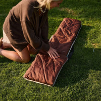 Brown striped outdoor mat laid on grass with person kneeling beside it