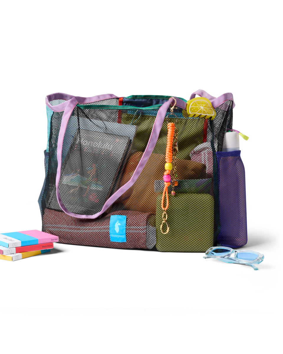 Iridescent mesh tote bag with purple handles and colorful accessories, styled with books and goggles