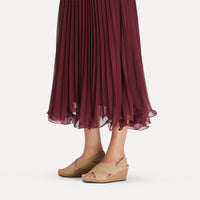 Tan leather wedge sandals with crossed straps and cork sole, worn with burgundy pleated skirt