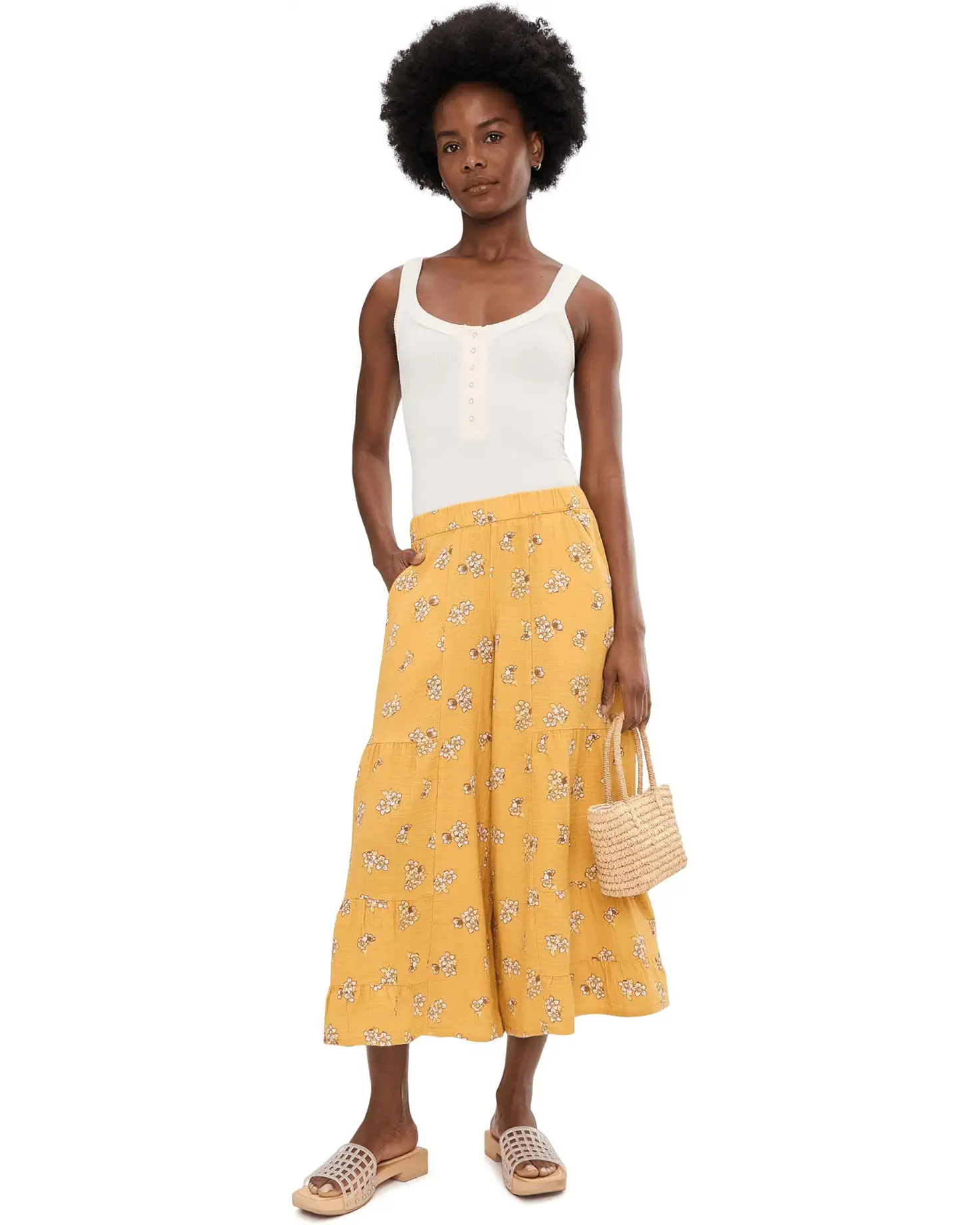 Woman wearing yellow floral palazzo pants with white tank top and woven bag