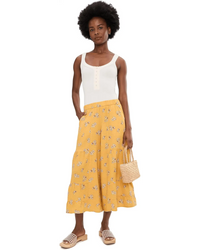 Woman wearing yellow floral palazzo pants with white tank top and woven bag