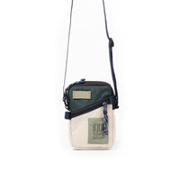 Small crossbody bag with green and cream color blocking, adjustable strap, front zipper pocket