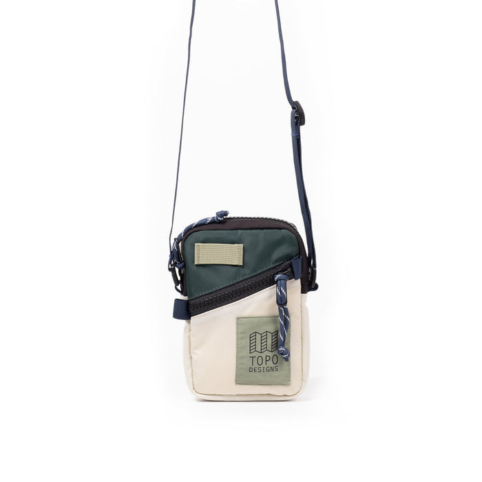Small crossbody bag with green and cream color blocking, adjustable strap, front zipper pocket