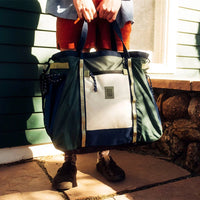Large duffel bag with forest green, white, and navy colorblocking being carried by person