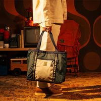 Two-tone utility tote bag with dark green and cream panels being carried in lifestyle setting