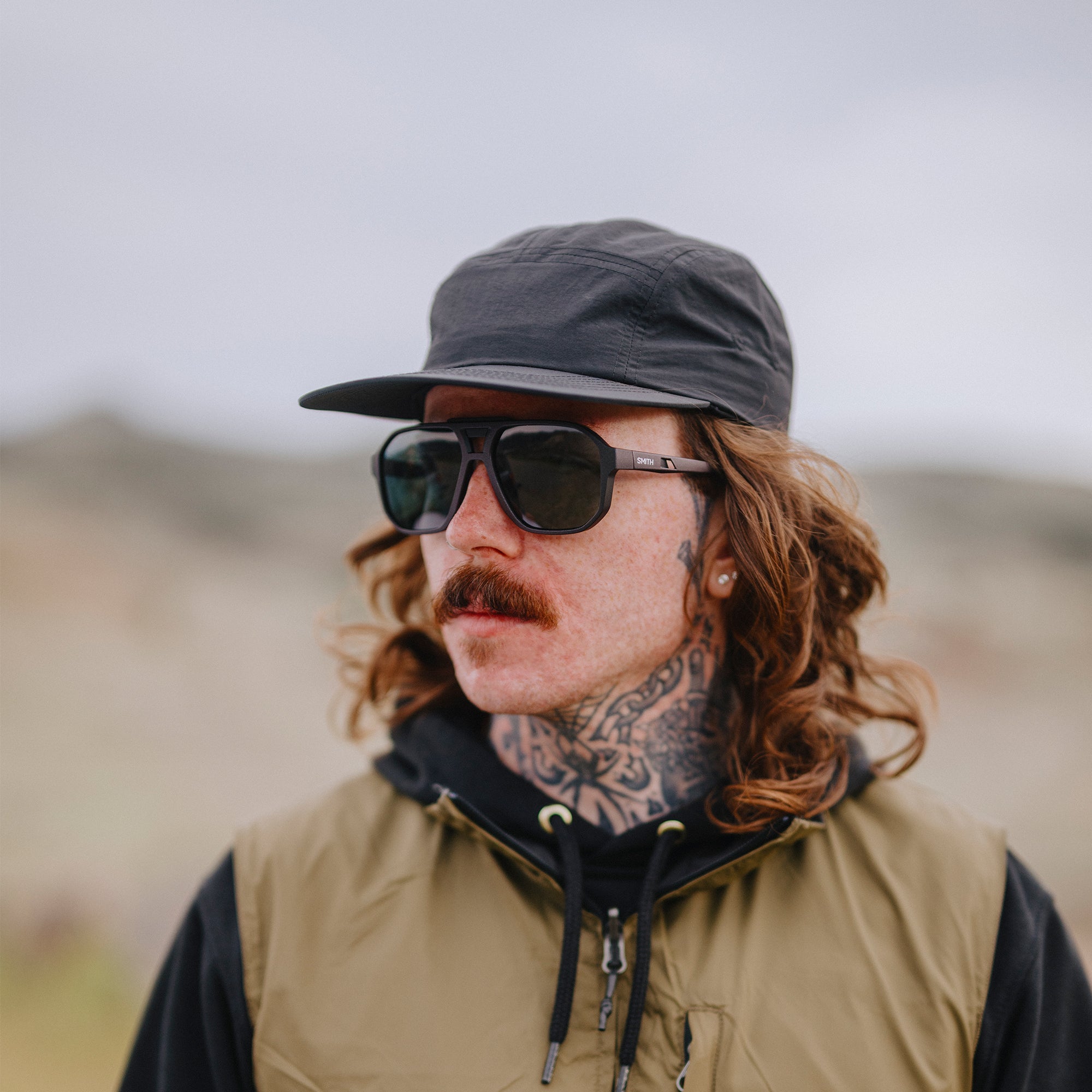 Dark-framed sunglasses worn by person with curly hair and mustache outdoors