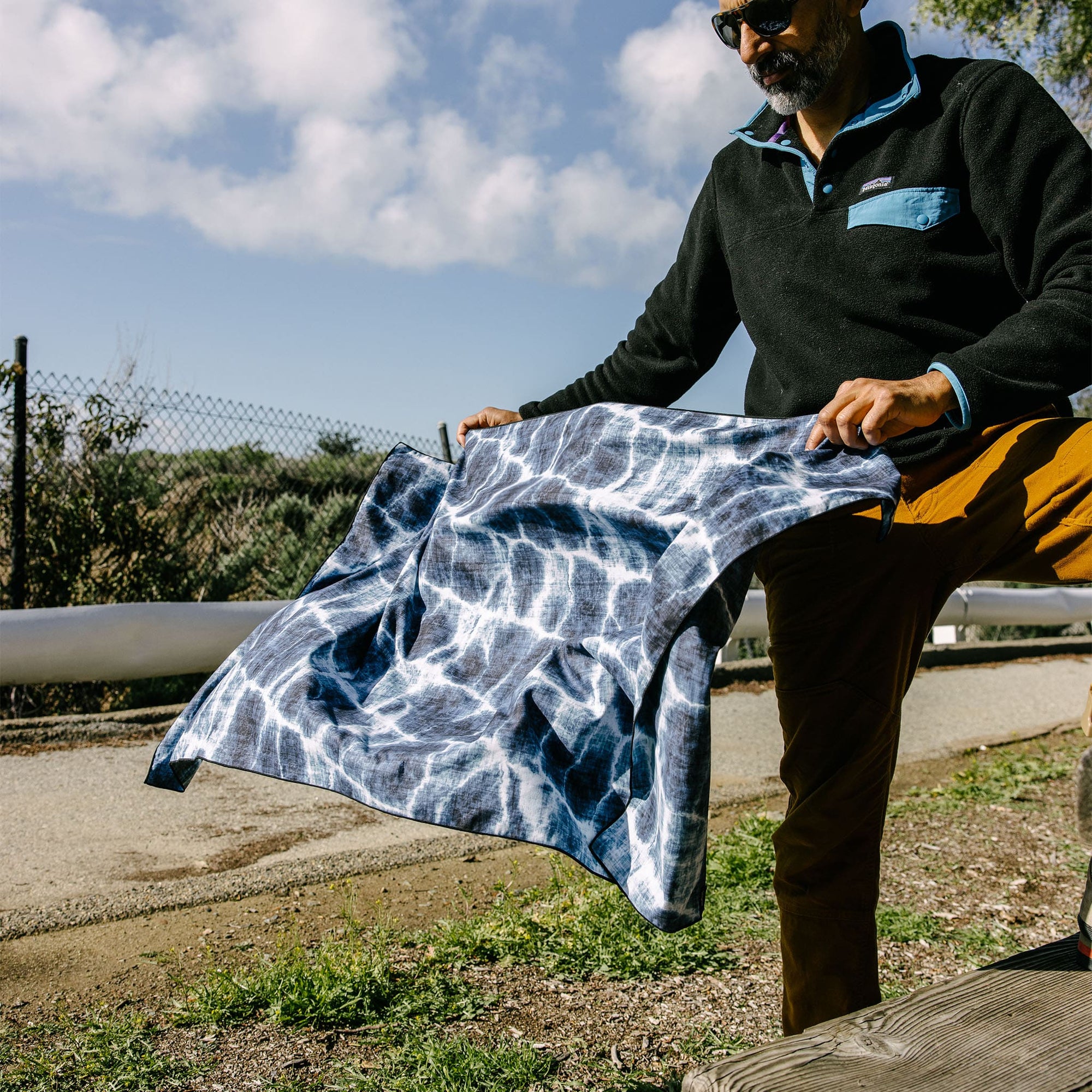 Blue and white patterned lightweight towel being held outdoors by person in casual wear