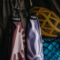 Purple ultralight towel with white daisy pattern hanging on mesh storage bag