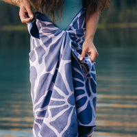 Purple patterned towel wrapped around waist being adjusted by hands near water