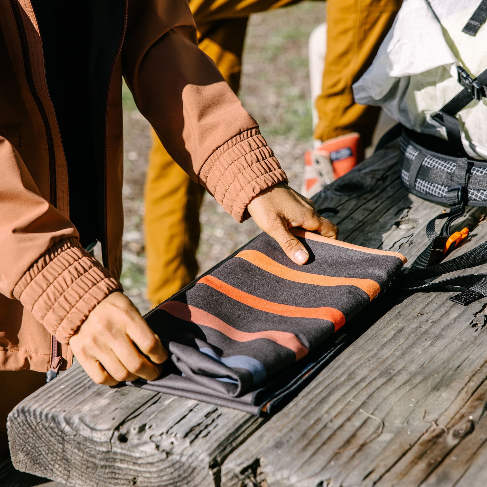 Compact travel towel with dark base and orange wavy stripes being packed into outdoor gear