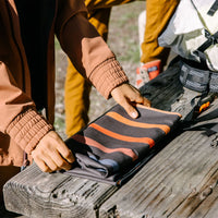 Compact travel towel with dark base and orange wavy stripes being packed into outdoor gear