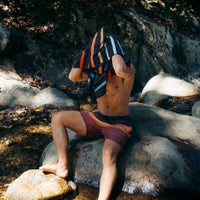 Striped quick-dry towel being held up by person sitting on rocky riverbank