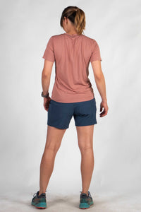 Woman wearing salmon pink athletic tee and navy shorts, back view showing fit