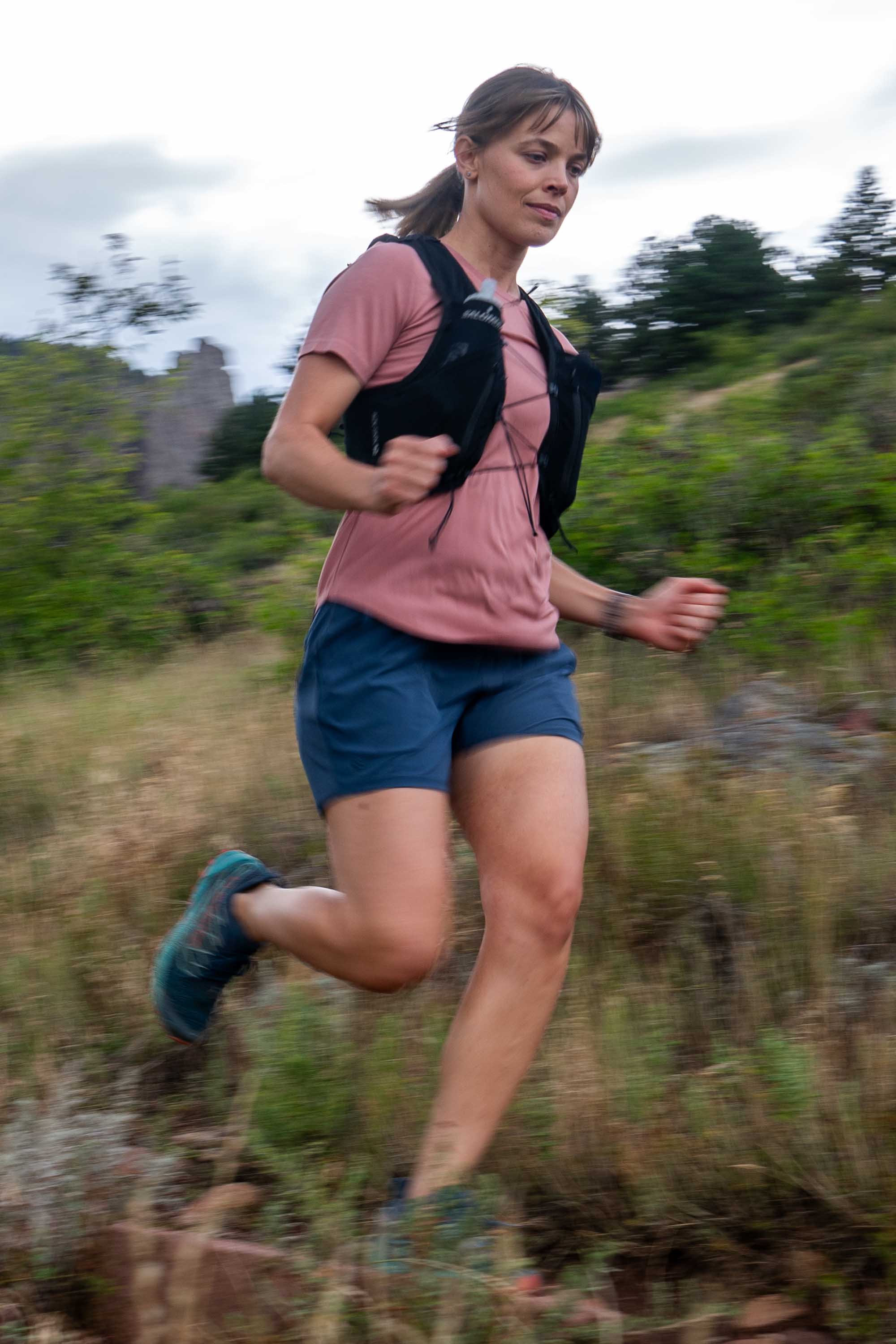 Woman running outdoors wearing pink athletic t-shirt with black vest, action shot