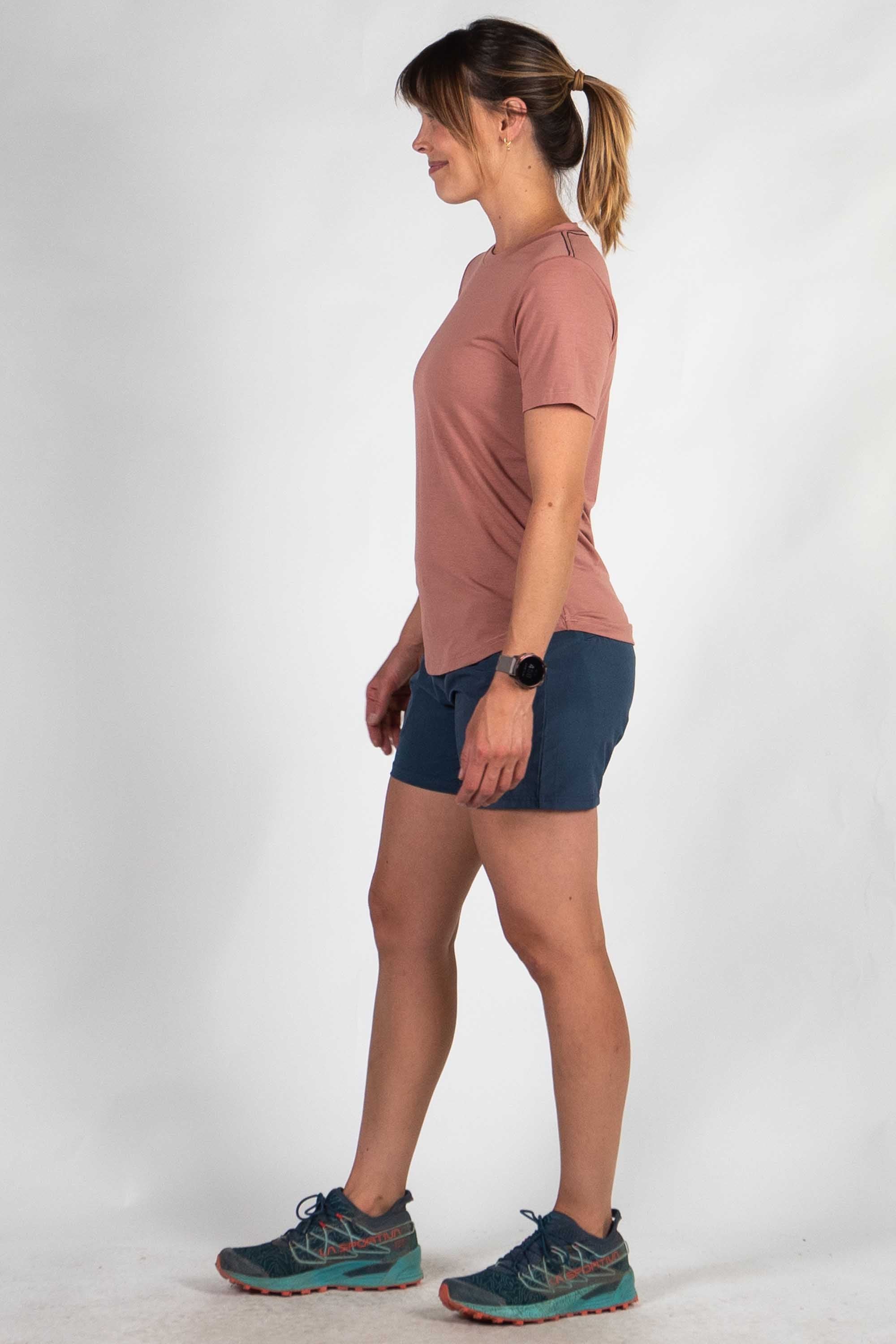 Woman wearing dusty rose athletic t-shirt and navy shorts, side profile view