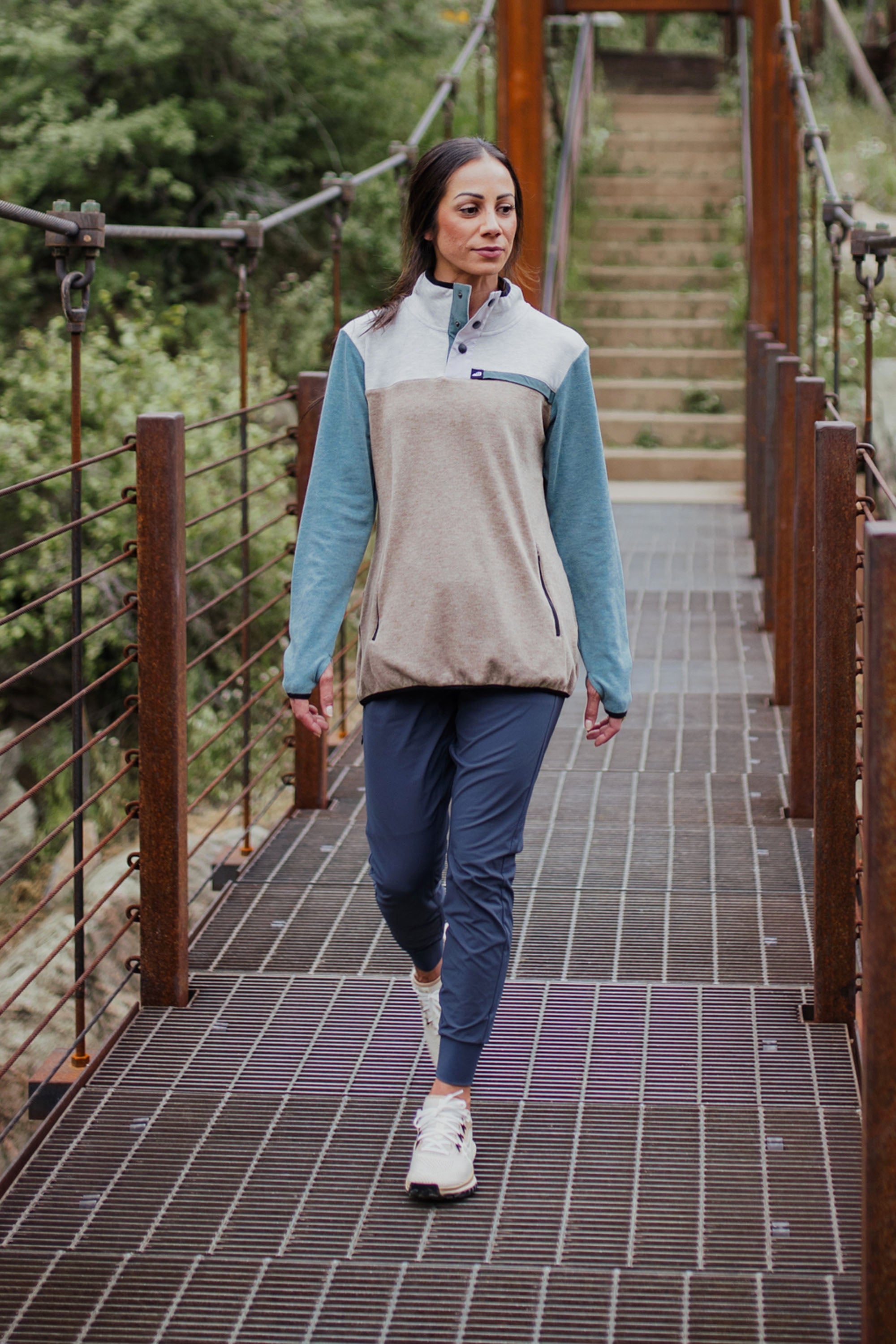 Woman walking on a suspension bridge wearing a color-block fleece pullover with teal sleeves and beige body