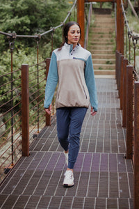Woman walking on a suspension bridge wearing a color-block fleece pullover with teal sleeves and beige body