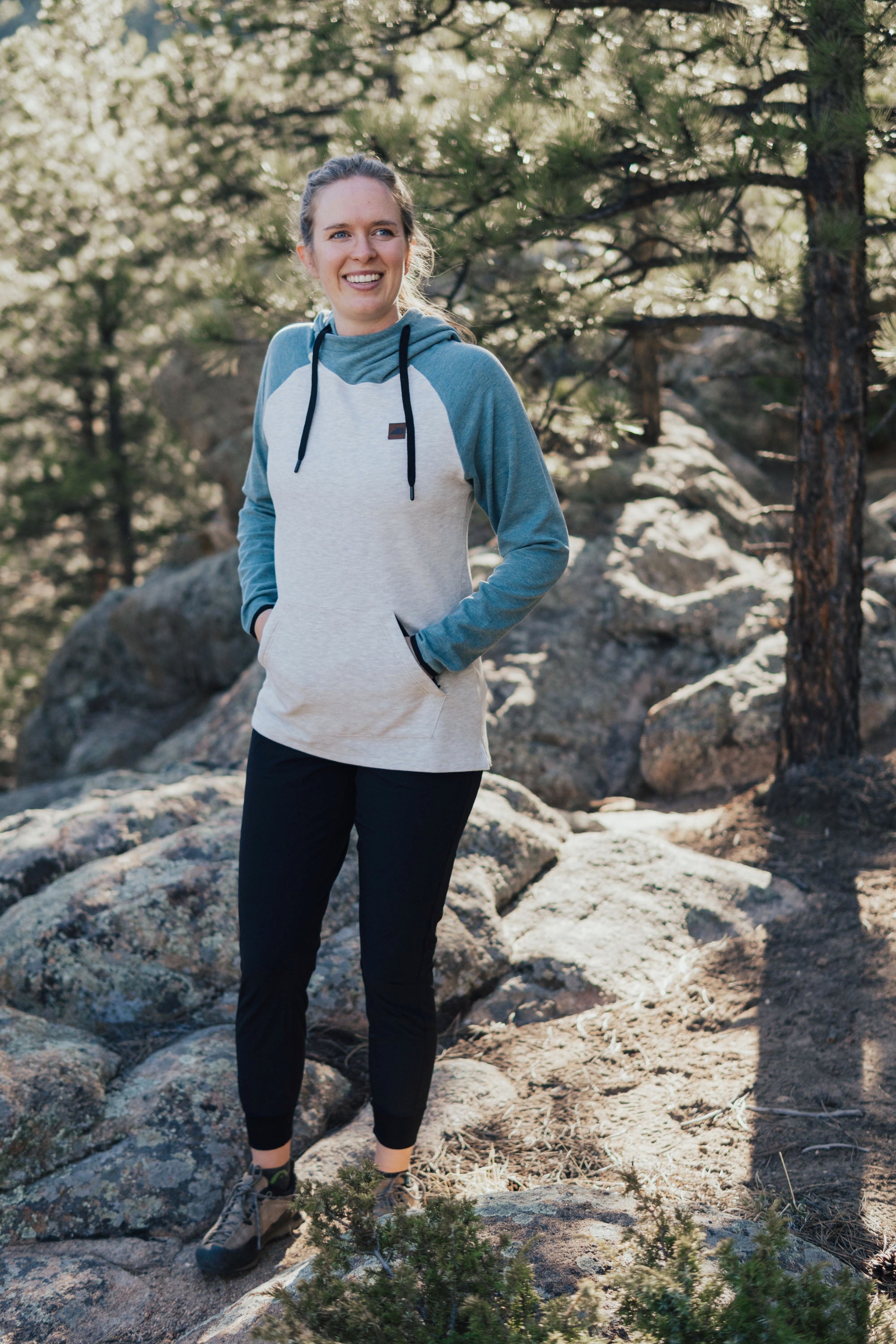 Women's fleece pullover hoodie with cream body and dusty blue raglan sleeves, worn outdoors
