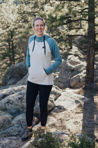 Women's fleece pullover hoodie with cream body and dusty blue raglan sleeves, worn outdoors